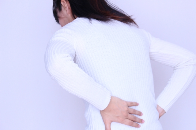 白い服を着て腰をおさえて前屈みになっている女性の画像