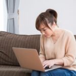 ソファでラップトップをいじる女性